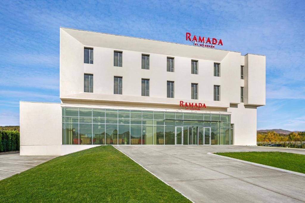 Fațada hotelului Ramada by Wyndham Târgu Jiu, cu intrarea vitrată și sigla hotelului.